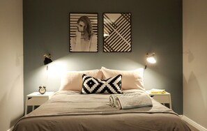 A neatly made bed with a patterned pillow, two bedside lamps, and a small table with a book and an alarm clock. - Spacious Townhouse - Netflix & Parking (Coventry)