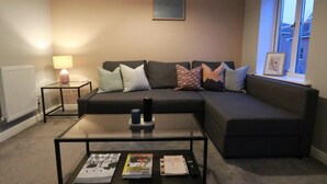 Ein modernes Wohnzimmer mit einem Ecksofa, einem Glastisch, einer Lampe und einem gerahmten Bild an der Wand.