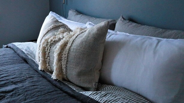 Ein Bett mit grauer Bettwäsche und einer weißen Strickdecke.