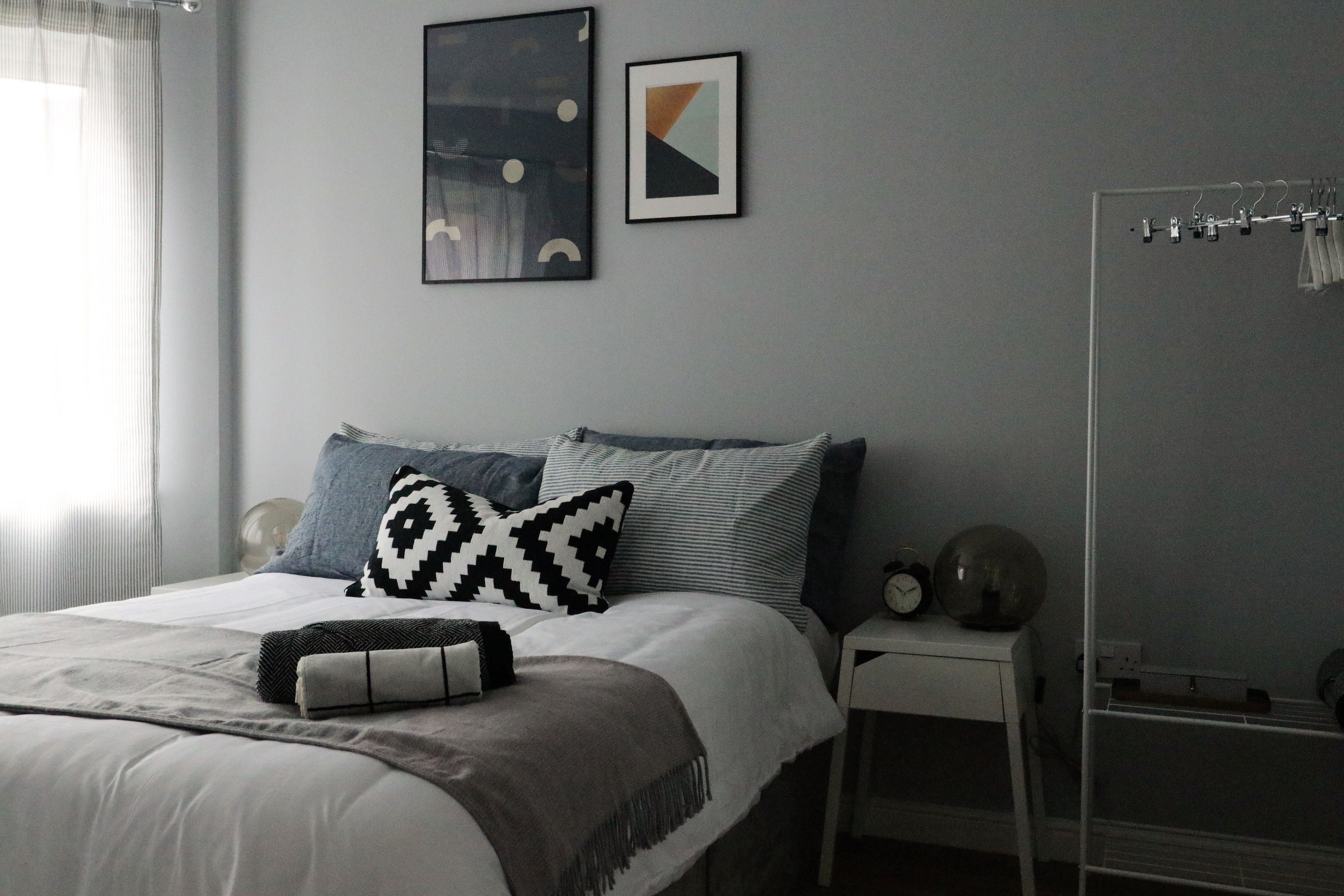 A neatly arranged bedroom with a bed, pillows, a bedside table with a clock, and a mirror.