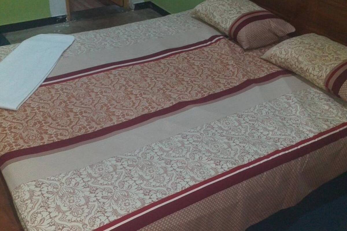 Ein Bett mit einem gemusterten Bettbezug, Kissen und einer Decke, sowie ein hölzernes Kopfstück.