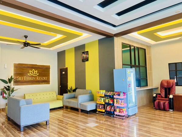 A reception area with a modern ceiling design, a clock, a sign for Sri Embun Resort, seating arrangements, and a refrigerator stocked with snacks.