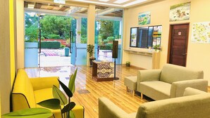 Un interior moderno con suelo de madera, sillas amarillas, sofás beige y una puerta de vidrio que da a un espacio exterior con vegetación.
