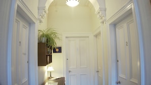 A hallway with white doors, a wooden shelf with a plant, and a desk with a lamp. - Barns Serviced Accommodation (Ayr)