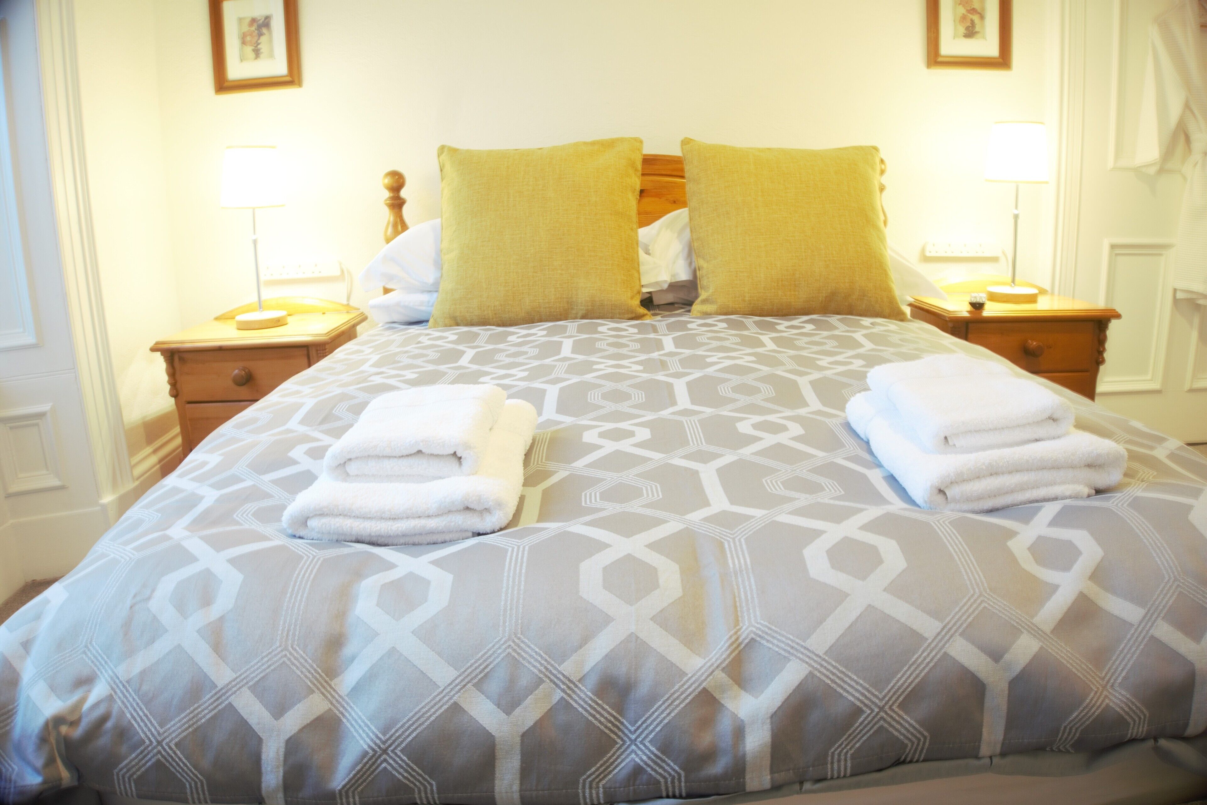 Een netjes opgemaakt bed met een sprei met geometrisch patroon, twee kussens en twee gevouwen handdoeken op het bed.