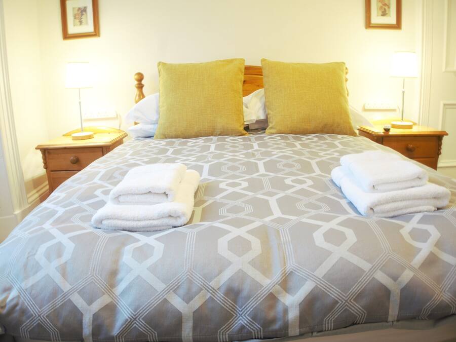 Een netjes opgemaakt bed met een sprei met geometrisch patroon, twee kussens en twee gevouwen handdoeken op het bed.