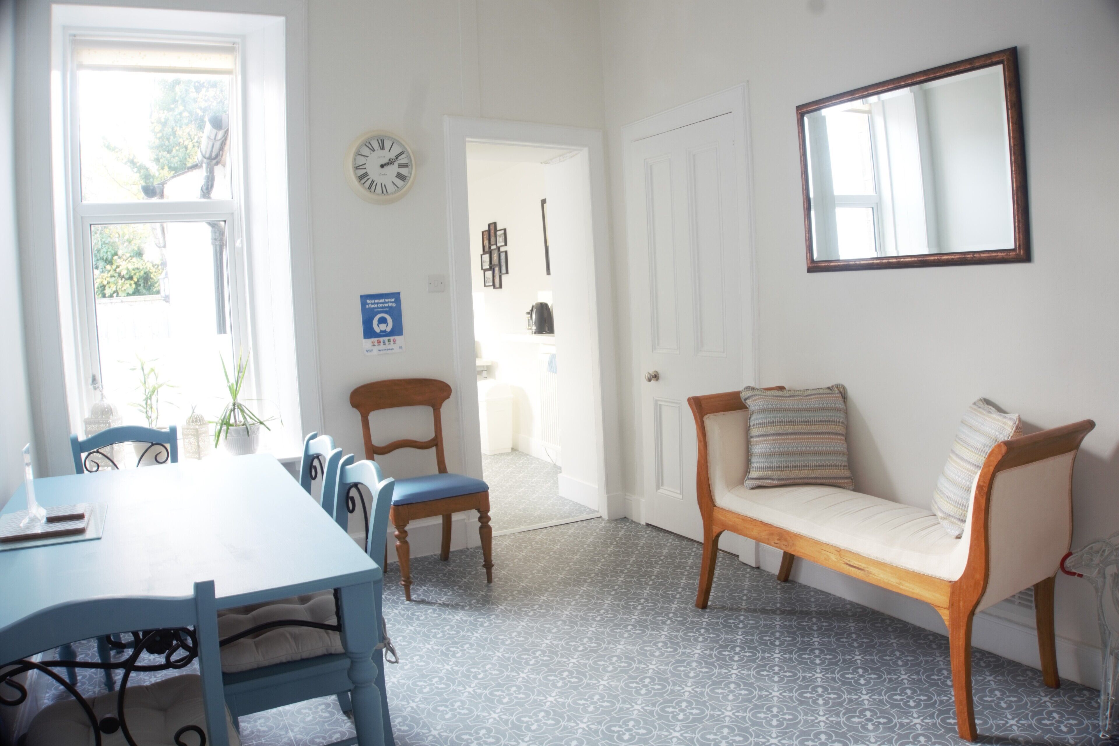 A dining area with a table and chairs, a bench, a clock, and a door leading to another room.