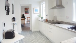 A modern kitchen with white cabinetry, a stainless steel range hood, and a window providing natural light. - Barns Serviced Accommodation (Ayr)