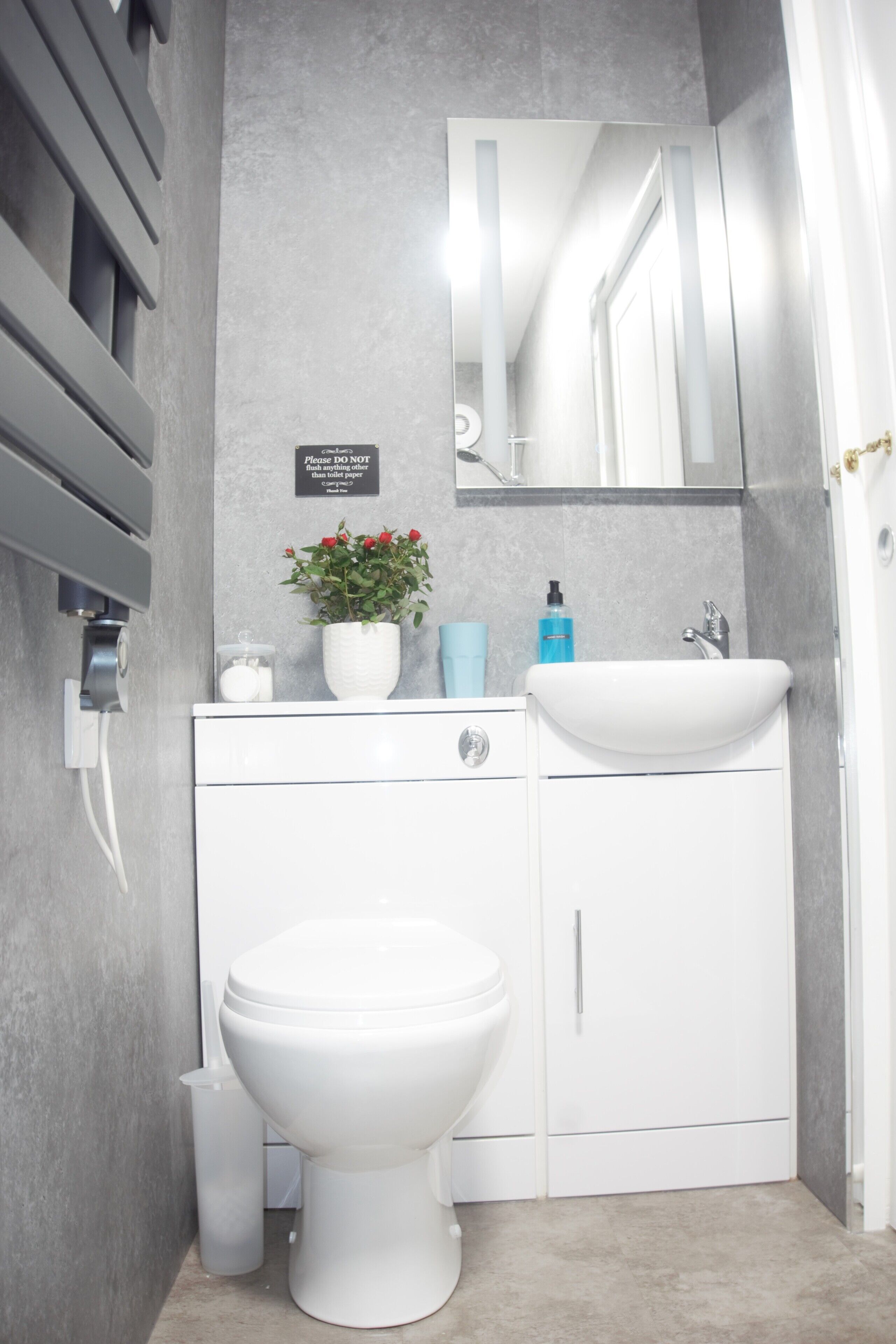 A modern bathroom with a white toilet, a sink, and a mirror above it. There is a sign on the wall and a potted plant on the counter.