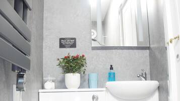 Un baño moderno con un inodoro blanco, un lavabo y un espejo encima. Hay un letrero en la pared y una planta en maceta sobre el mostrador.