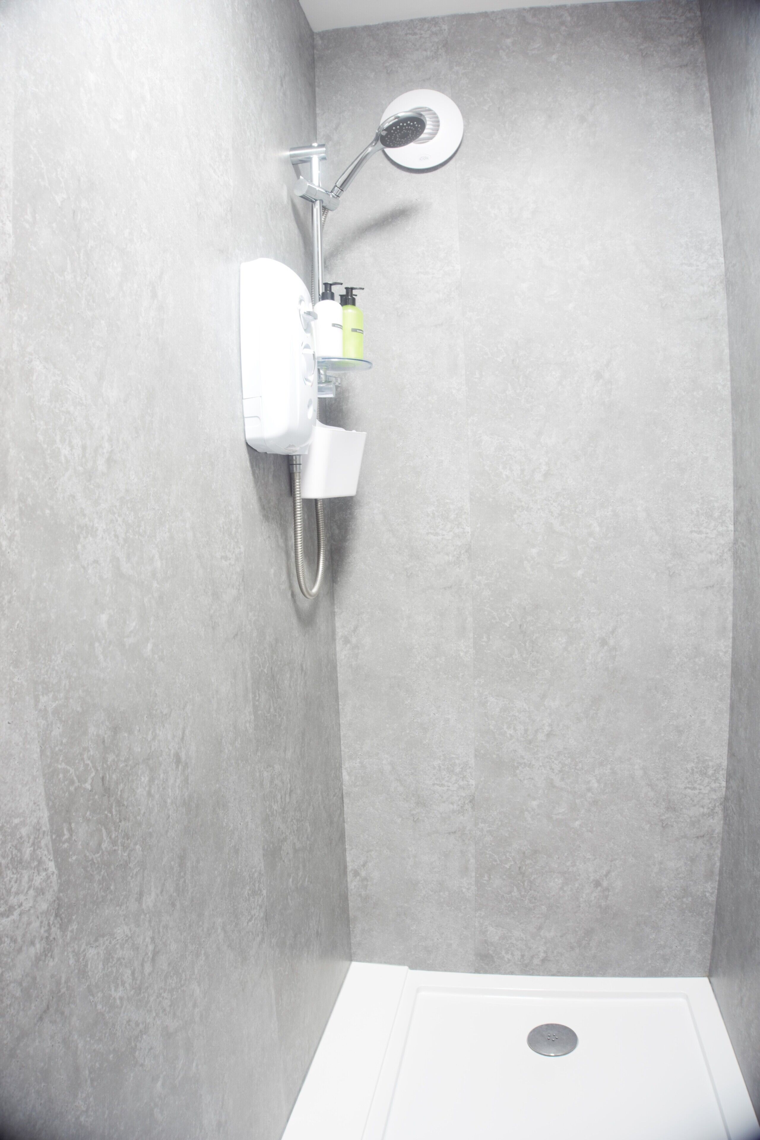 A shower with a handheld showerhead, a wall-mounted control panel, and a white sink with a mirror.