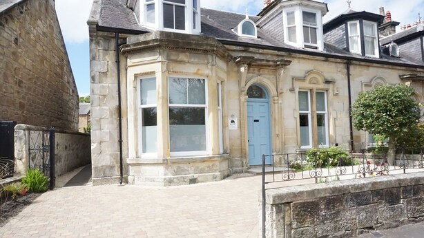 A historic stone building with a blue door, large windows, and a brick pathway leading to the entrance. - Barns Serviced Accommodation (Ayr)