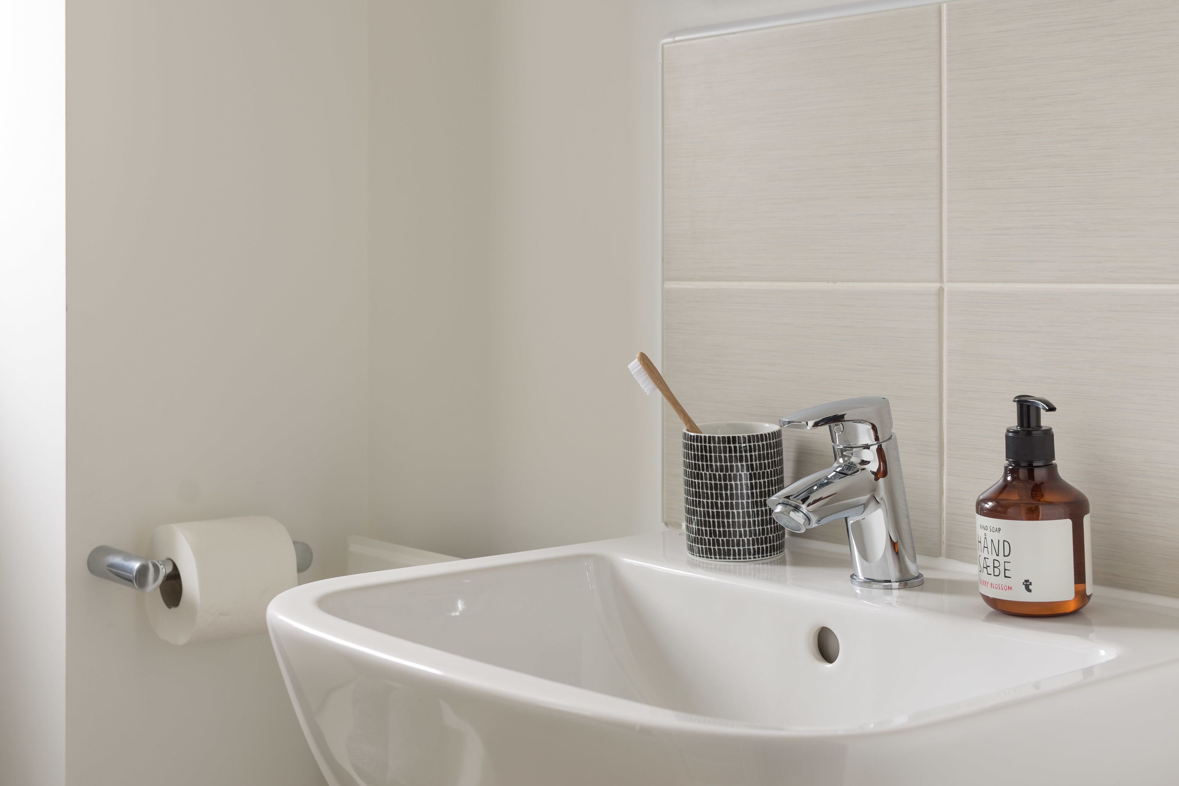 A bathroom sink with a white basin, a silver faucet, a black and white mug, and a bottle of hand soap.
