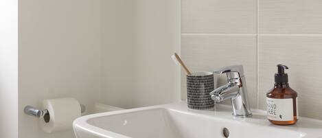 A bathroom sink with a white basin, a silver faucet, a black and white mug, and a bottle of hand soap.
