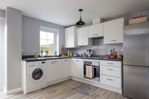 A modern kitchen with white cabinets, a stainless steel refrigerator, a built-in washing machine, and a window providing natural light.