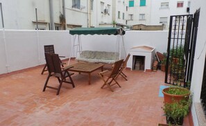 Eine Terrasse mit Tisch, Stühlen und einer kleinen Couch, sowie einem grünen Sonnensegel.