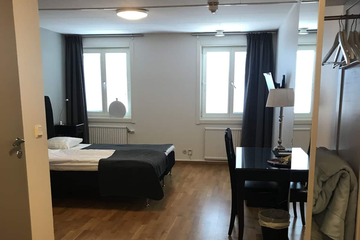 A hotel room with two beds, a desk, a chair, a lamp, and a coat rack.