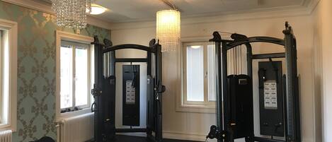 A gym with two weightlifting stations, a chandelier, and patterned wallpaper.