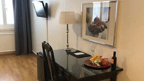 A dining area with a table, chairs, a lamp, a framed picture, a trash bin, and a TV on the wall. - Hotell Gustaf (Götene)