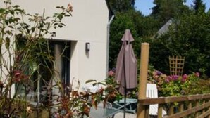 A white building with a small window, a wooden fence, and a garden with various plants and flowers. - Land / Sea / Landes- Pink Granite Coast (Perros-Guirec)
