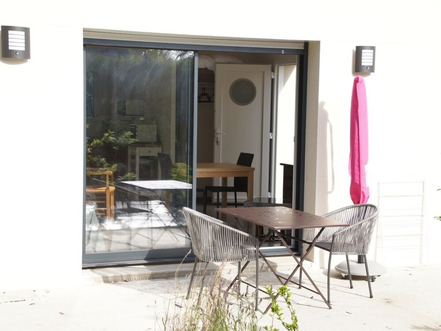 Eine Terrasse im Freien mit Tisch und zwei Stühlen, einer Glastür zum Verschieben und einem rosa Handtuch an der Wand.