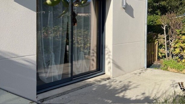 A modern building with a large sliding glass door, a small window, and a concrete pathway leading to the entrance. - Land / Sea / Landes- Pink Granite Coast (Perros-Guirec)