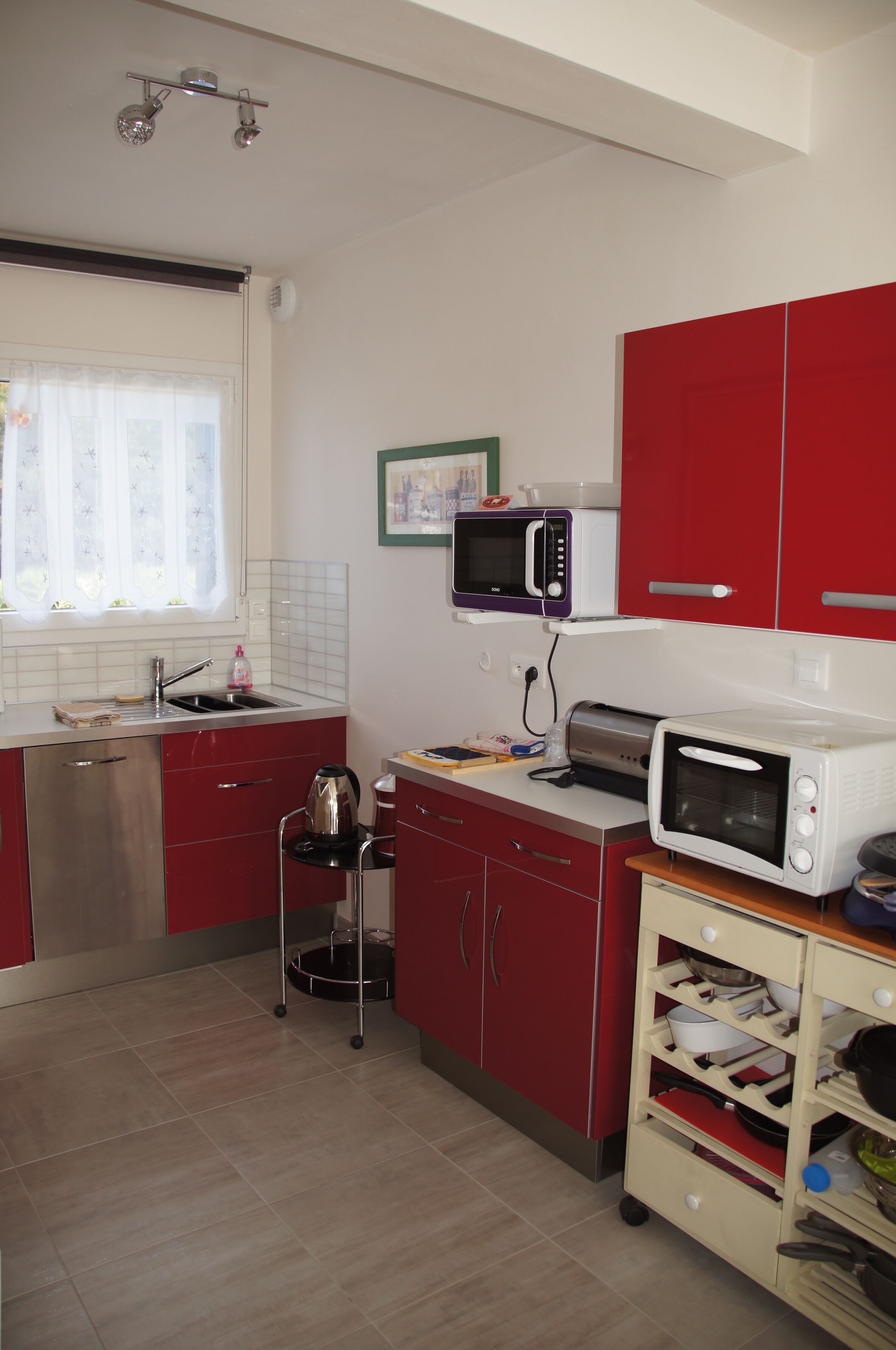 A compact kitchen with red cabinets, a stainless steel dishwasher, a microwave, and a toaster.