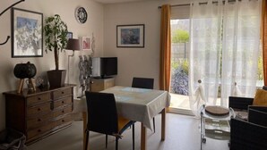 A dining area with a table, chairs, a TV, and a window with curtains. - Land / Sea / Landes- Pink Granite Coast (Perros-Guirec)