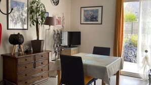 A room with a dining table, chairs, a TV, a plant, and artwork on the walls. - Land / Sea / Landes- Pink Granite Coast (Perros-Guirec)