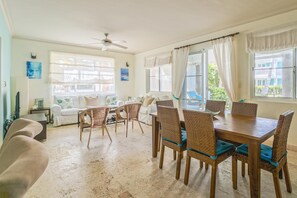 A dining area with a wooden table and wicker chairs, a ceiling fan, and large windows with curtains. - Playa Turquesa P105_200Mbps_Private Beach Access_BBQ_Pools (Bavaro-Punta Cana)
