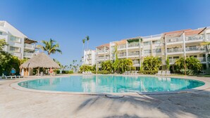 Una piscina rodeada por una zona de resort con edificios de varios pisos, palmeras y sillas de descanso.