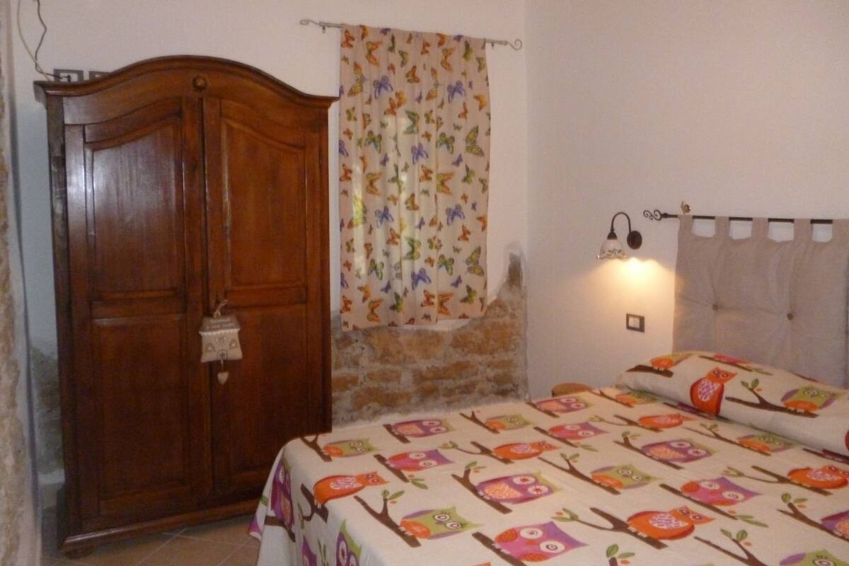 Ein Schlafzimmer mit einem Holzschrank, einem Bett mit einer Bettdecke mit Eule-Muster, einem Vorhang mit Schmetterlingsmotiv und einer Wandlampe.