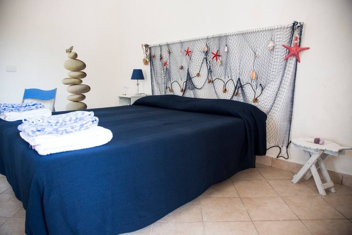 Ein Zimmer mit einem Bett, einem Sessel, einem kleinen Tisch und einer Wanddekoration.