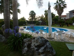 A swimming pool with white lounge chairs, surrounded by palm trees and a rock. - La Taverna dei Ciucci Bed & Breakfast (Capaccio-Paestum)