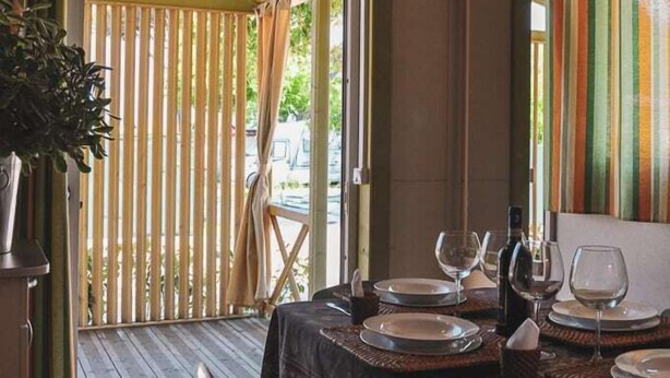 Un coin repas avec une table dressée pour quatre personnes, une plante en pot et une vue sur l’extérieur par une porte.