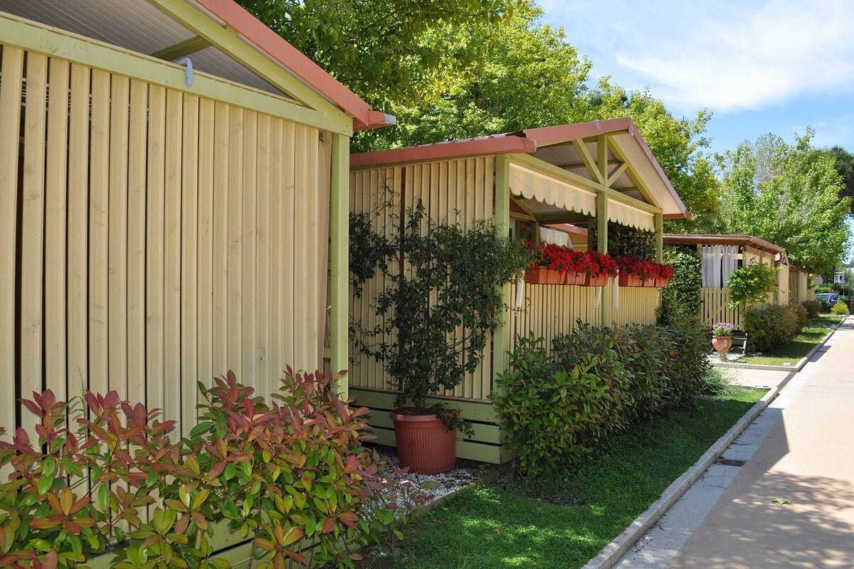 Une rangée de cabanes en bois, chacune dotée d’une véranda, entourée de jardins et d’arbres bien entretenus.