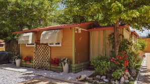 Une petite construction en bois, avec un toit rouge, une véranda et un jardin agrémenté de fleurs rouges.