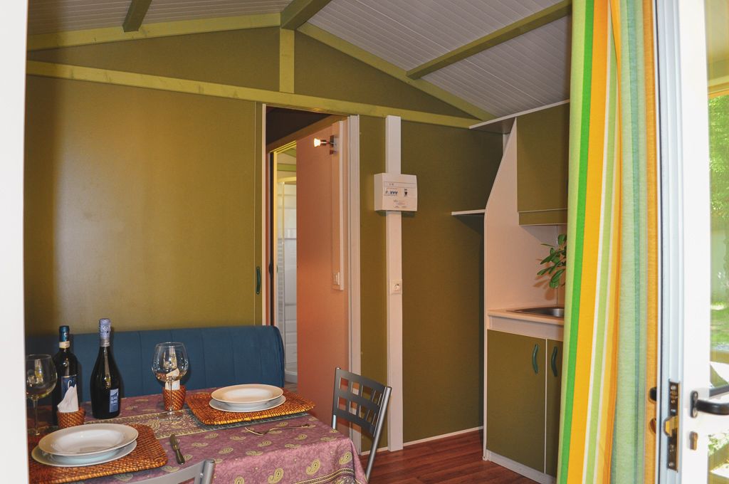 Een eetruimte met een tafel voor twee personen, een bank en een keuken die zichtbaar is door een open deur.