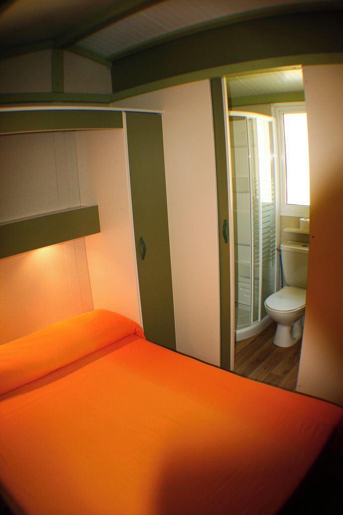 A compact room with a single bed, a shower area, and a toilet.