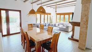 Un comedor espacioso con mesa y sillas de madera, un conjunto de sofás y ventanas amplias que dejan entrar luz natural.
