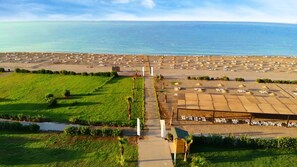 Vista aèria d'un complex turístic amb files de gandules i ombrelles, una vista clara del mar i una zona enjardinada ben cuidada.