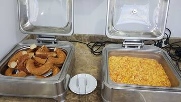 Two stainless steel food dispensers with lids open, one containing sliced bagels and the other filled with a yellowish food item, on a marble countertop.