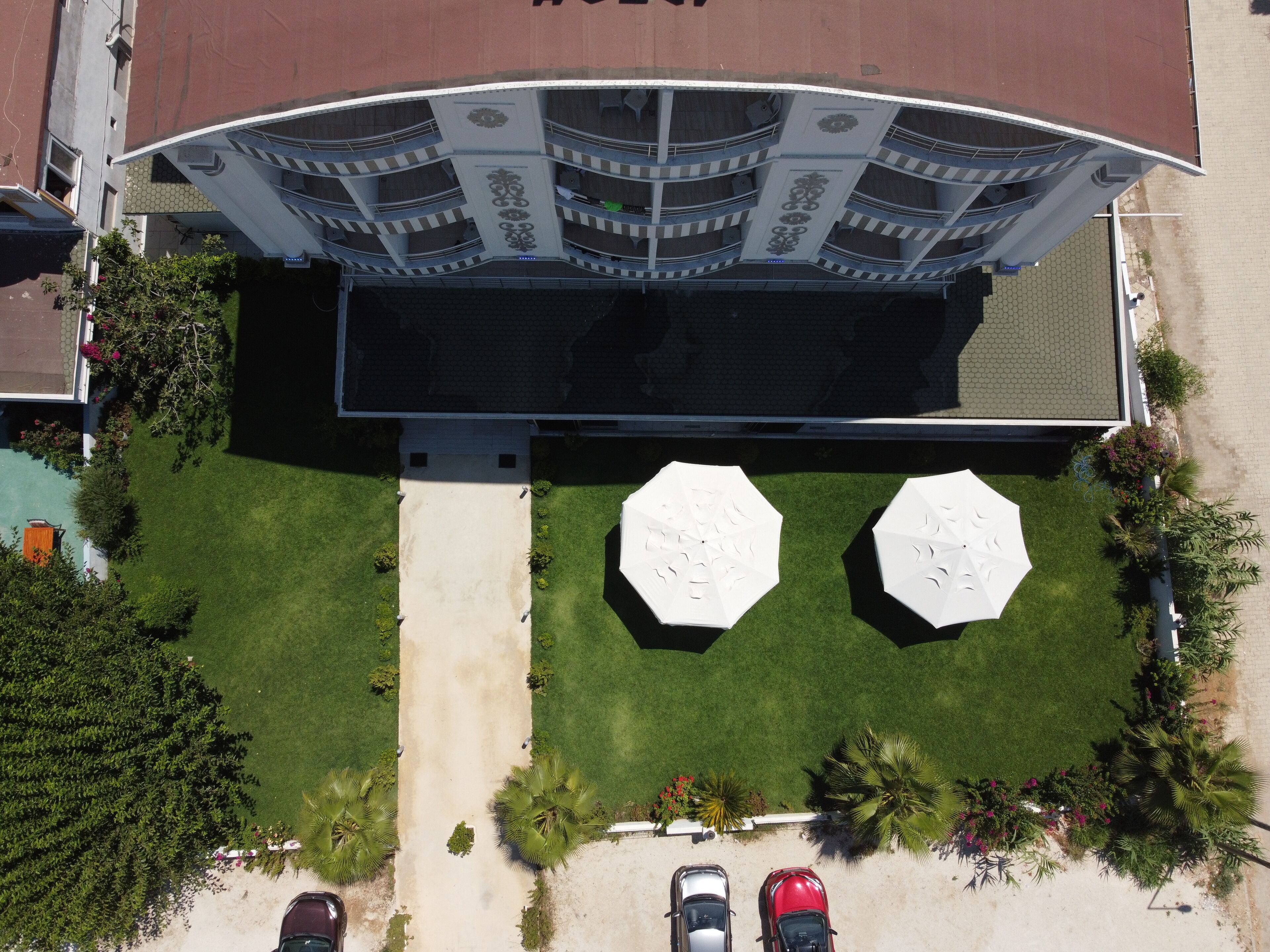 Vista aérea de un hotel con un patio central, dos parasoles grandes y un estacionamiento con coches.