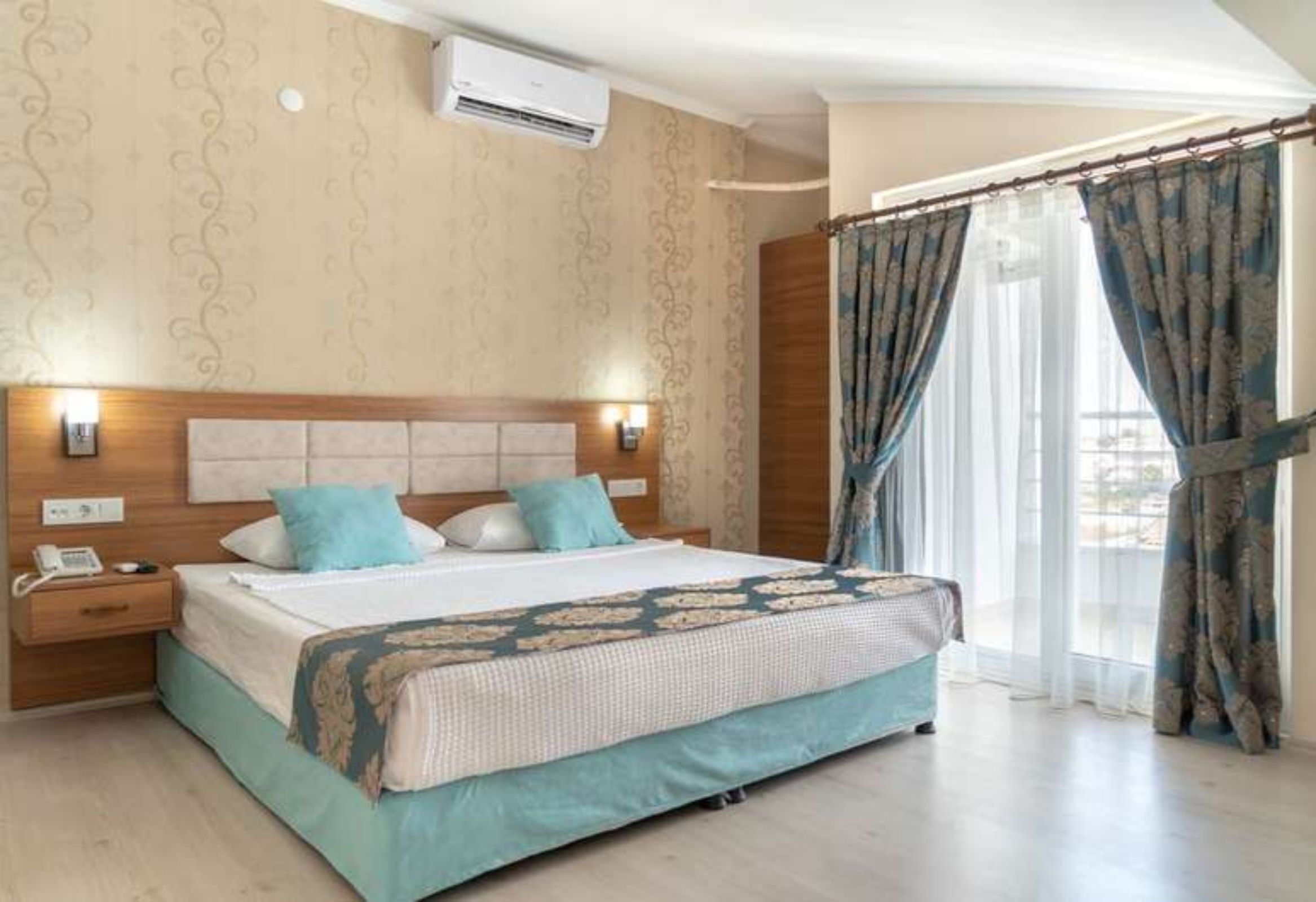 A hotel room with a large bed, a wooden headboard, a bedside table with a phone, and a window with curtains.