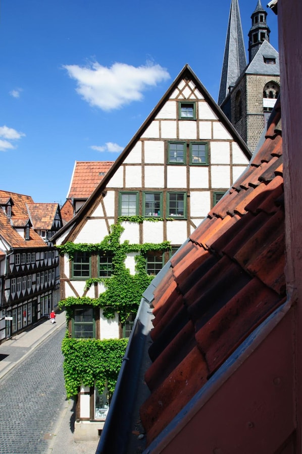 Un bâtiment traditionnel à colombages, doté d’un toit à forte pente et dont le clocher d’une église est visible en arrière-plan.