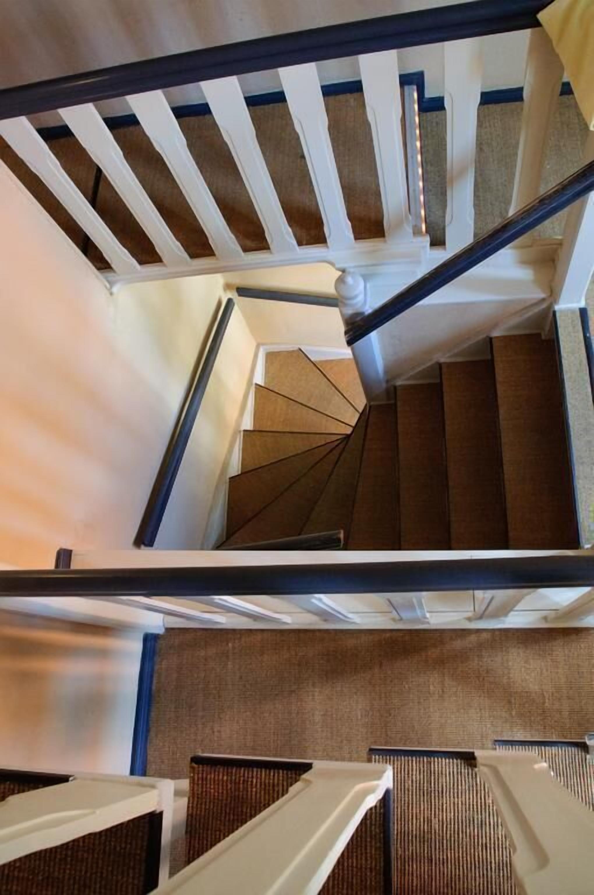 A staircase with white balusters and a dark handrail, leading to a landing with a patterned carpet.