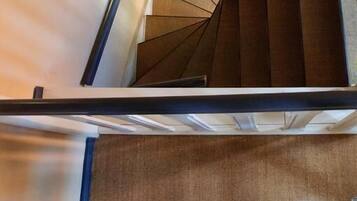 A staircase with white balusters and a dark handrail, leading to a landing with a patterned carpet.