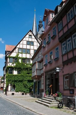 Eine Kopfsteinpflasterstraße gesäumt von traditionellen europäischen Gebäuden, darunter eine Kirche mit einem Kirchturm und ein Haus mit einem Balkon.