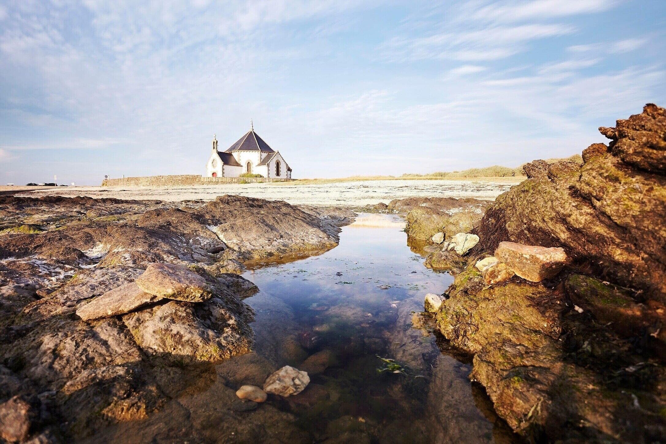Un paysage côtier avec une église blanche, un terrain rocheux et un petit plan d’eau.