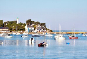 A marina with various boats docked, a lighthouse in the background, and buildings along the shore. - Character apartment between Ocean and Gulf in a charming property. (Arzon)